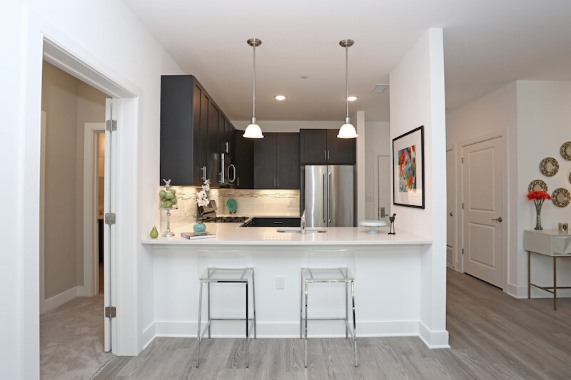 Modern gourmet kitchen with quartz waterfall peninsula, dark cabinetry, stainless appliances, glass tile backsplash, and pendant lighting