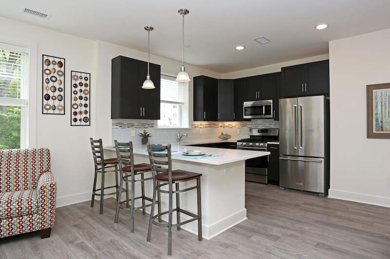 Gourmet kitchen with quartz breakfast bar, dark custom cabinetry, stainless French-door refrigerator, gas range, and pendant lighting